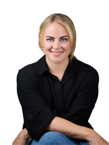 Smiling blonde woman wearing a black shirt and jeans, arms crossed, against a white background.